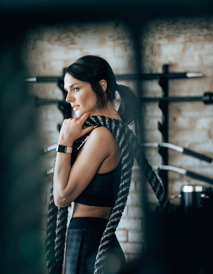 A woman in a gym with a battle rope over her shoulder, a watch on her wrist.