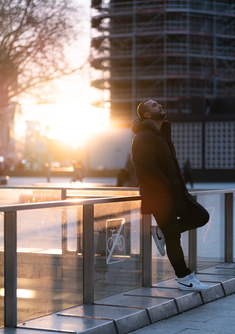 A man leaning on a railing in low sunrise light, head tipped back.